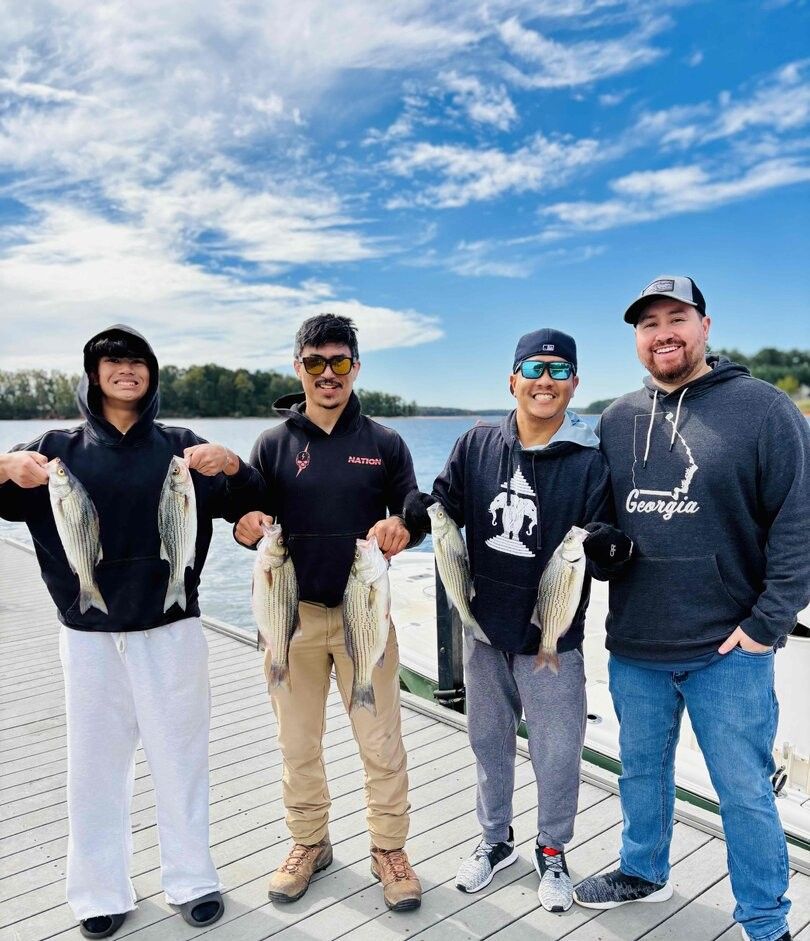 Four anglers displaying their striped bass catch on a wooden dock