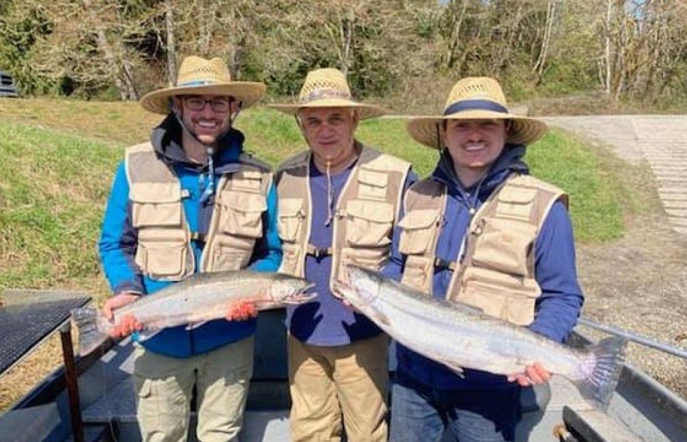 Three anglers in fishing gear displaying caught fish on boat