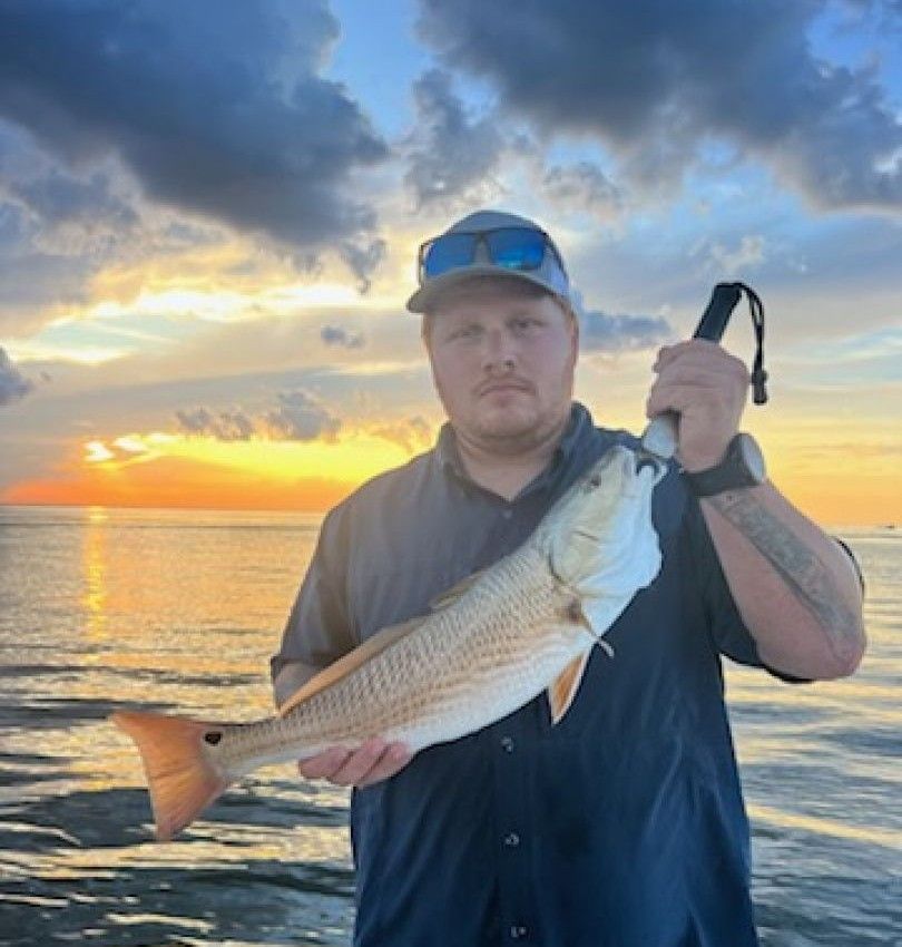 Angler holding caught redfish during sunset on water