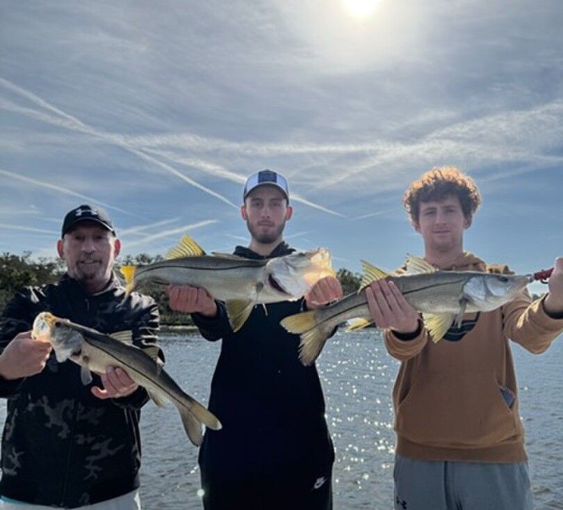 Three anglers displaying their caught snook fish on the water