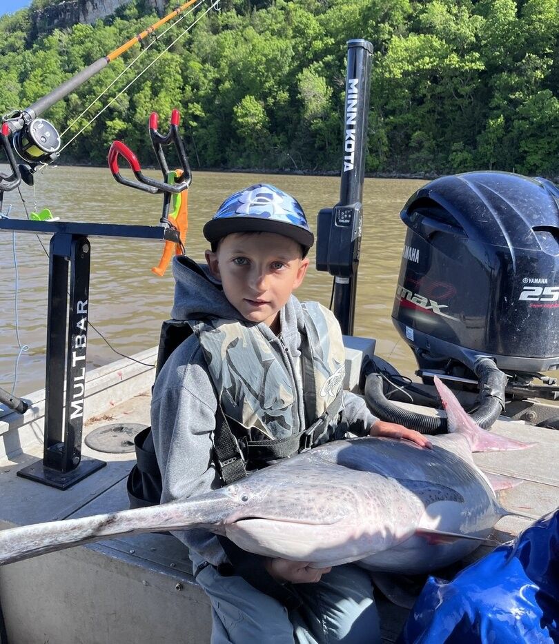 Large catfish caught during fishing trip on muddy river with boat and fishing equipment visible