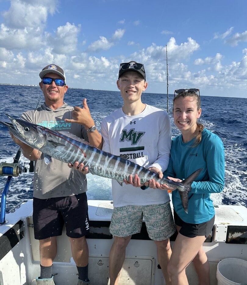 Three people on fishing boat holding freshly caught wahoo fish on ocean