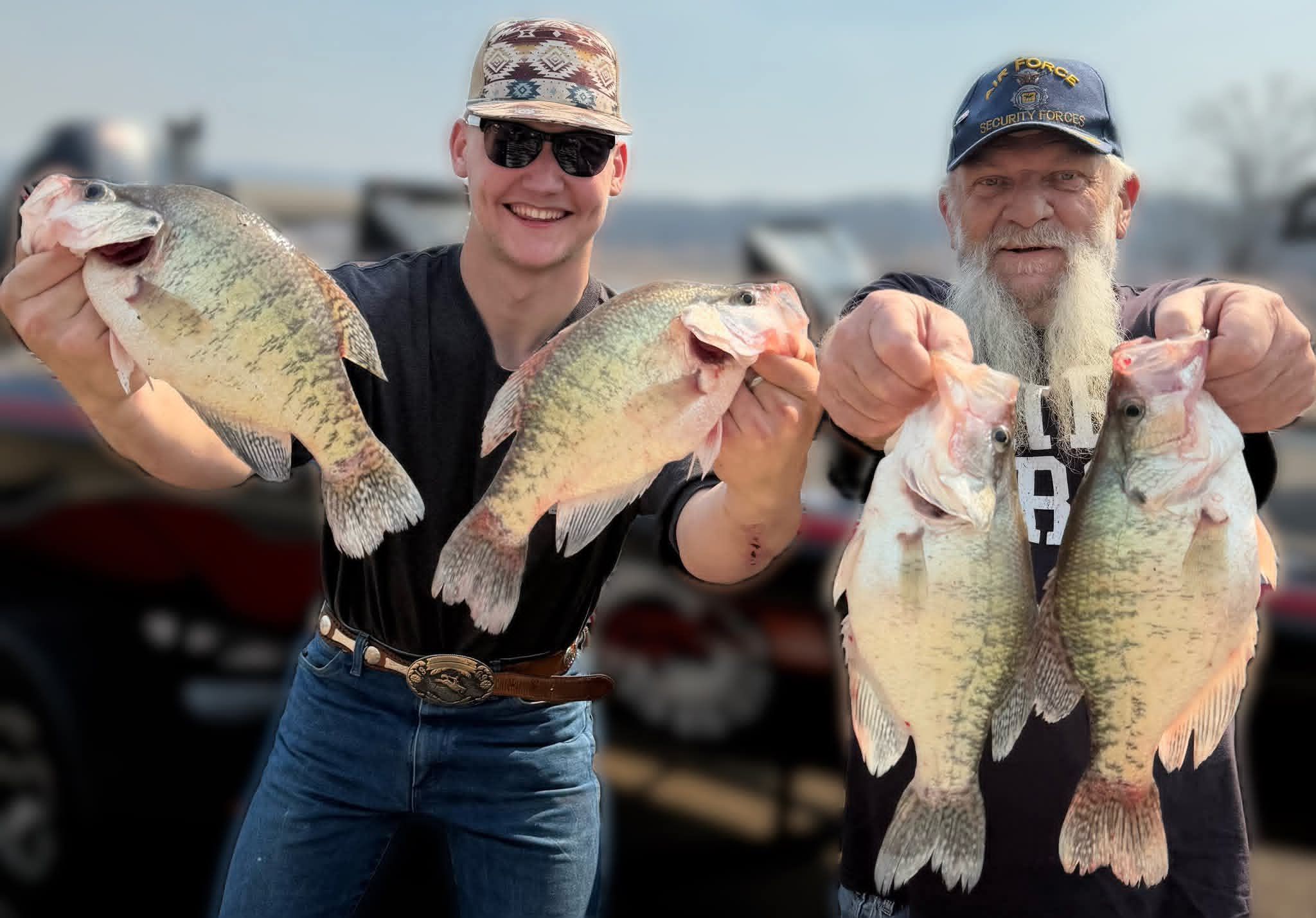 Two anglers displaying their catch of four bass fish at a marina