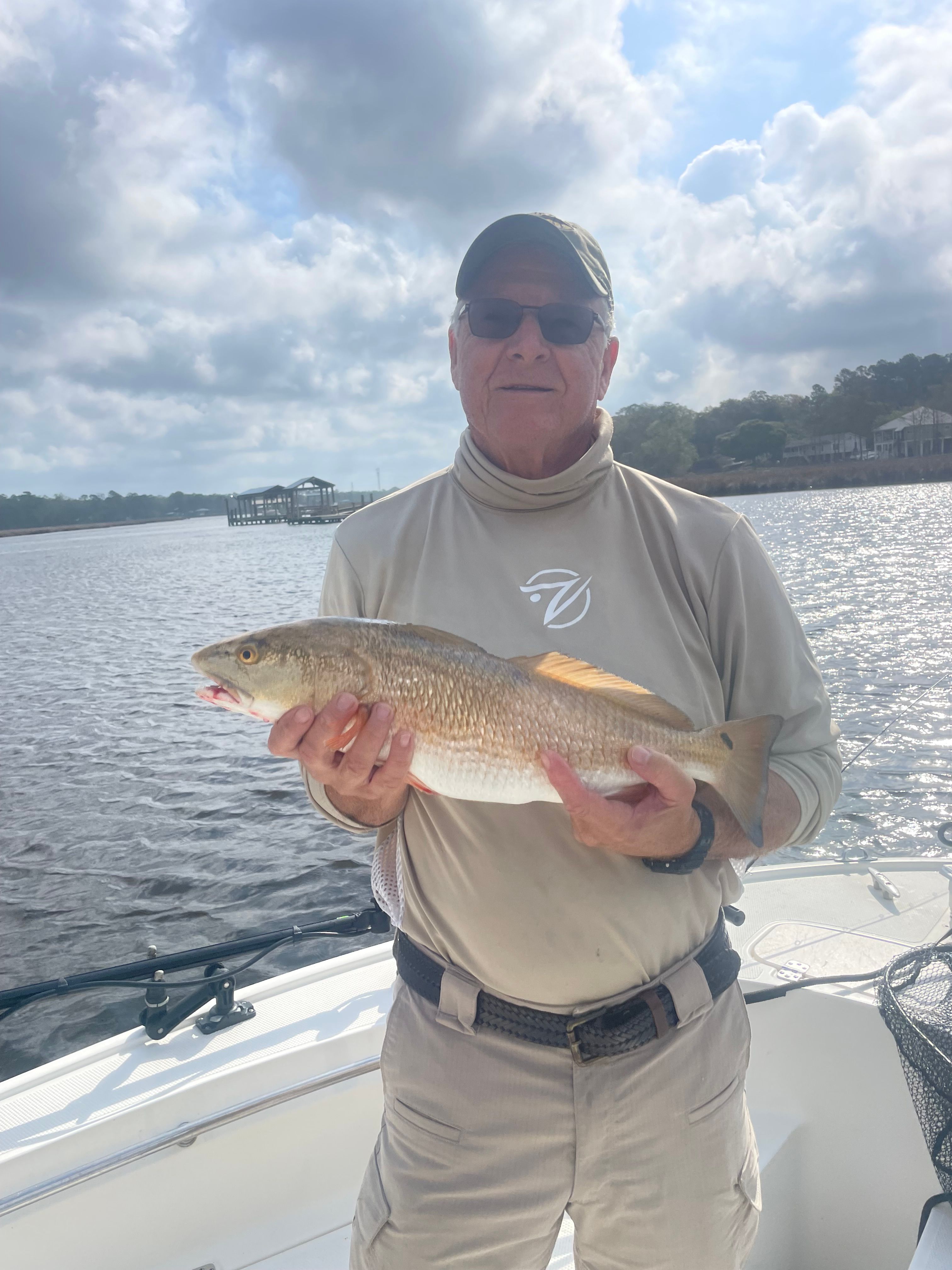 Angler holding a caught redfish on a fishing boat with water and shoreline in background
