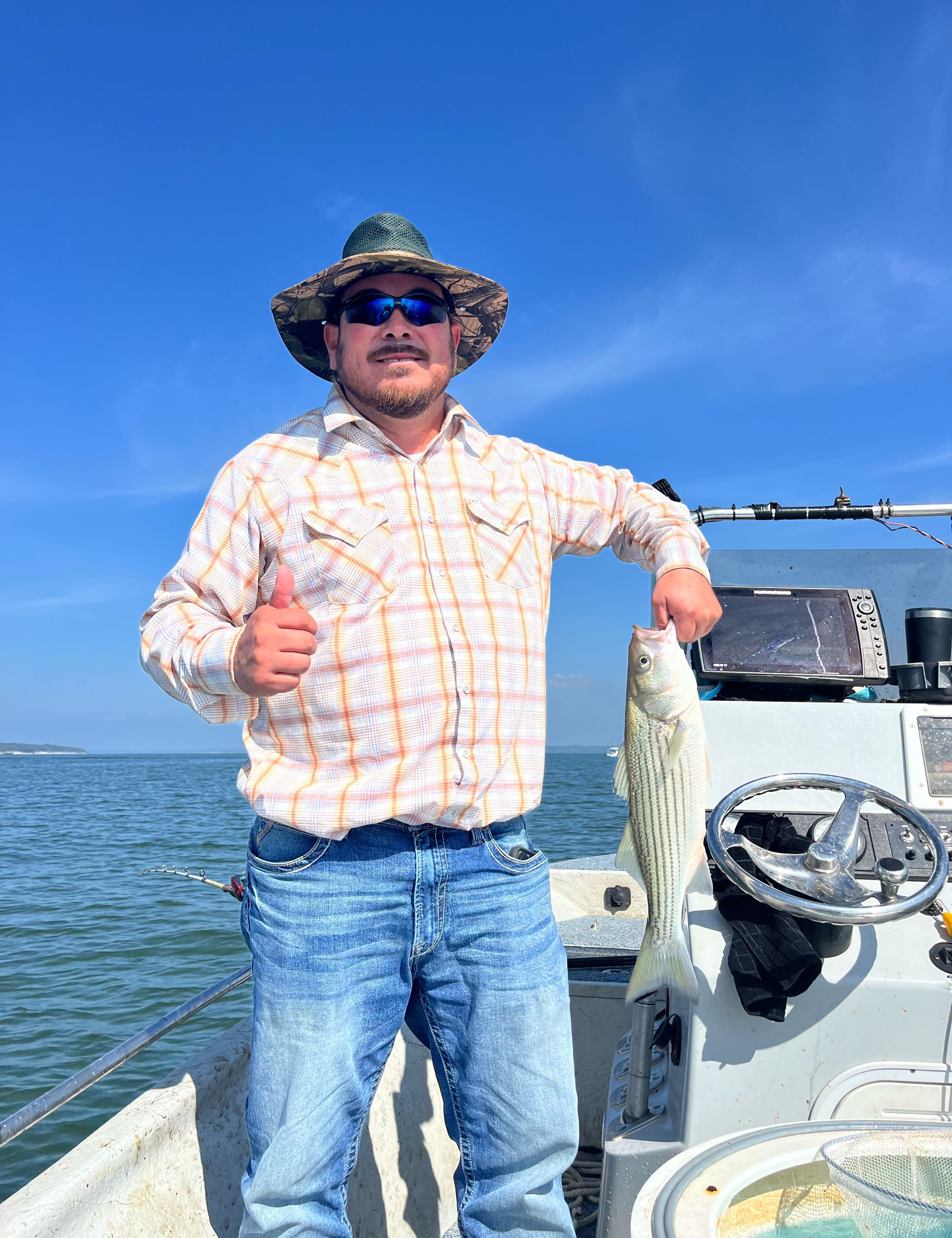 Freshly caught striped bass displayed on fishing boat with clear blue sky and ocean waters