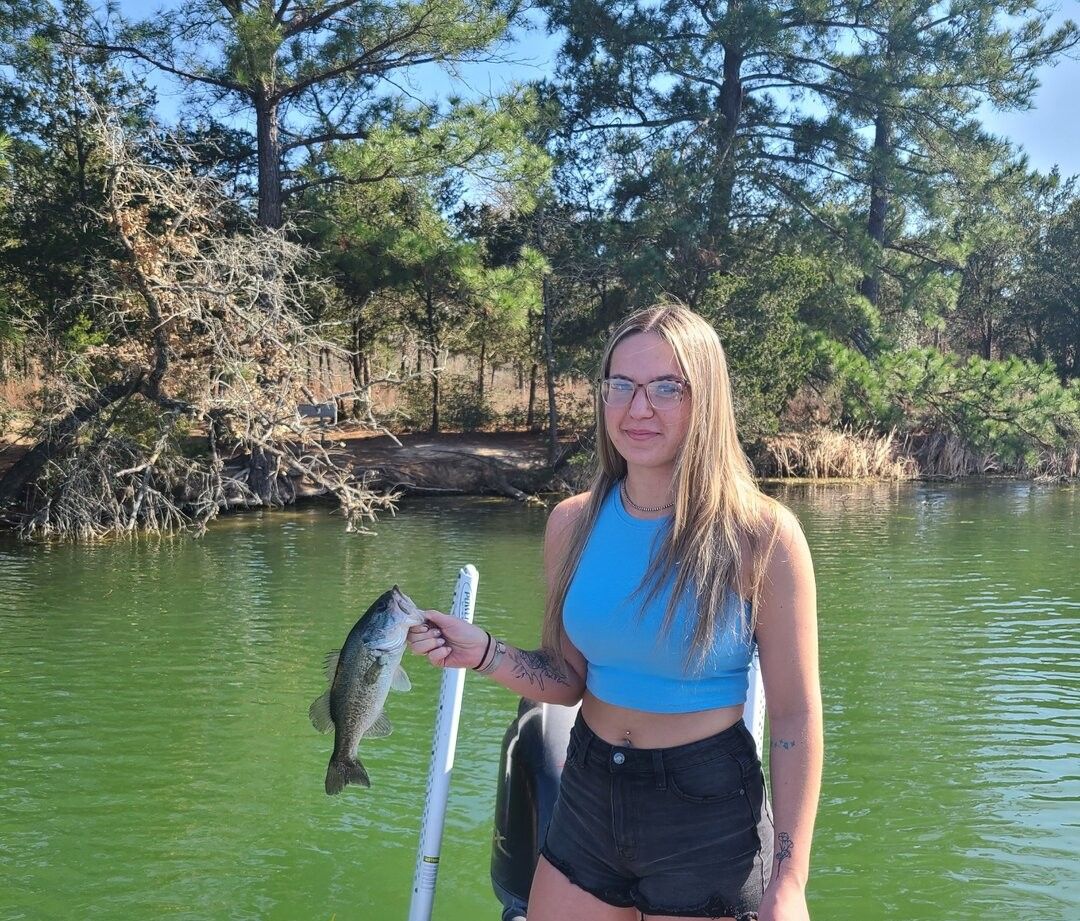 Bass fish caught while fishing, held next to measuring ruler at lake with trees in background