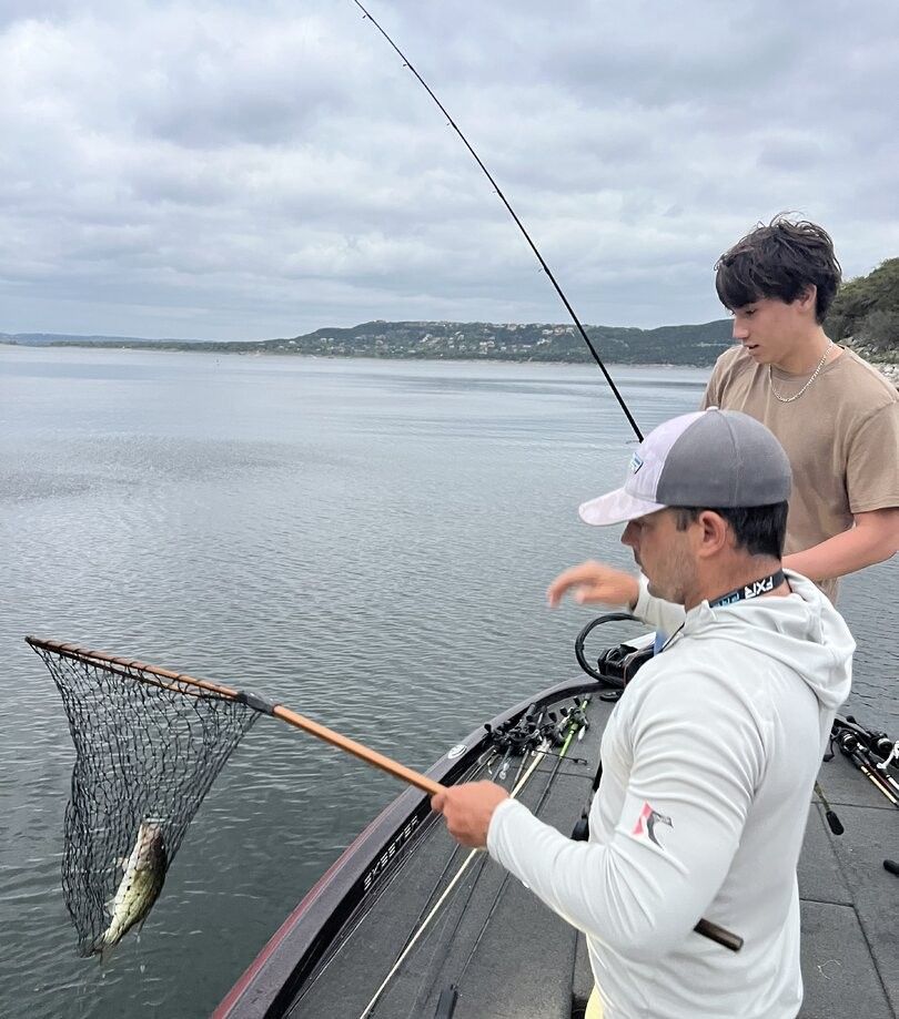 Bass fishing from boat with fishing rod and landing net on calm lake water