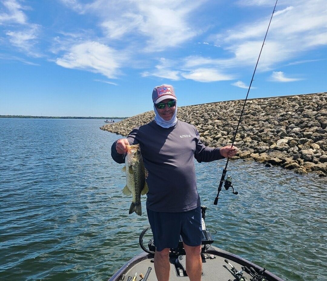 Angler holding caught bass fish on boat near rocky shoreline
