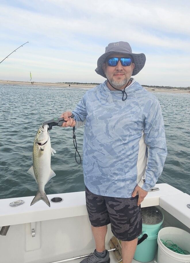 Angler holding freshly caught bluefish on fishing boat deck with ocean water in background