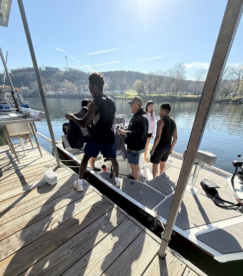 Group preparing fishing boat at marina dock with calm water and wooded hills in background