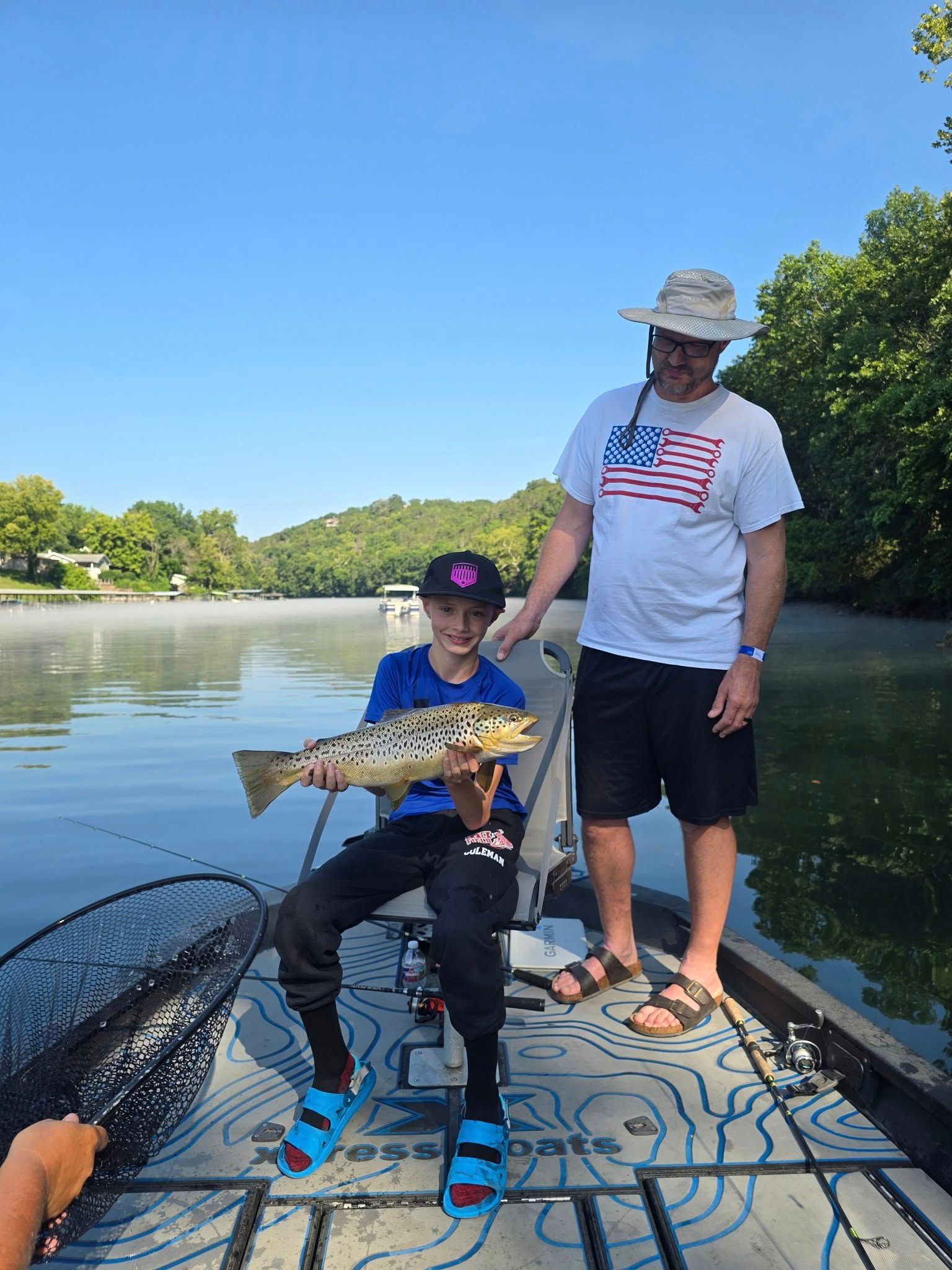 Brown trout catch displayed on fishing boat deck with lake and forested hills in background