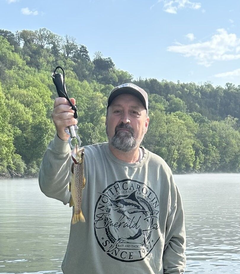 Angler holding brown trout caught while fishing on lake surrounded by forested hills