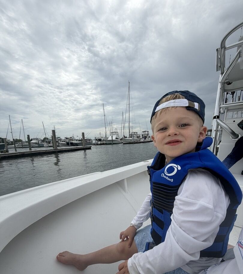 Young child on boat deck at marina with sailboats and yachts in background