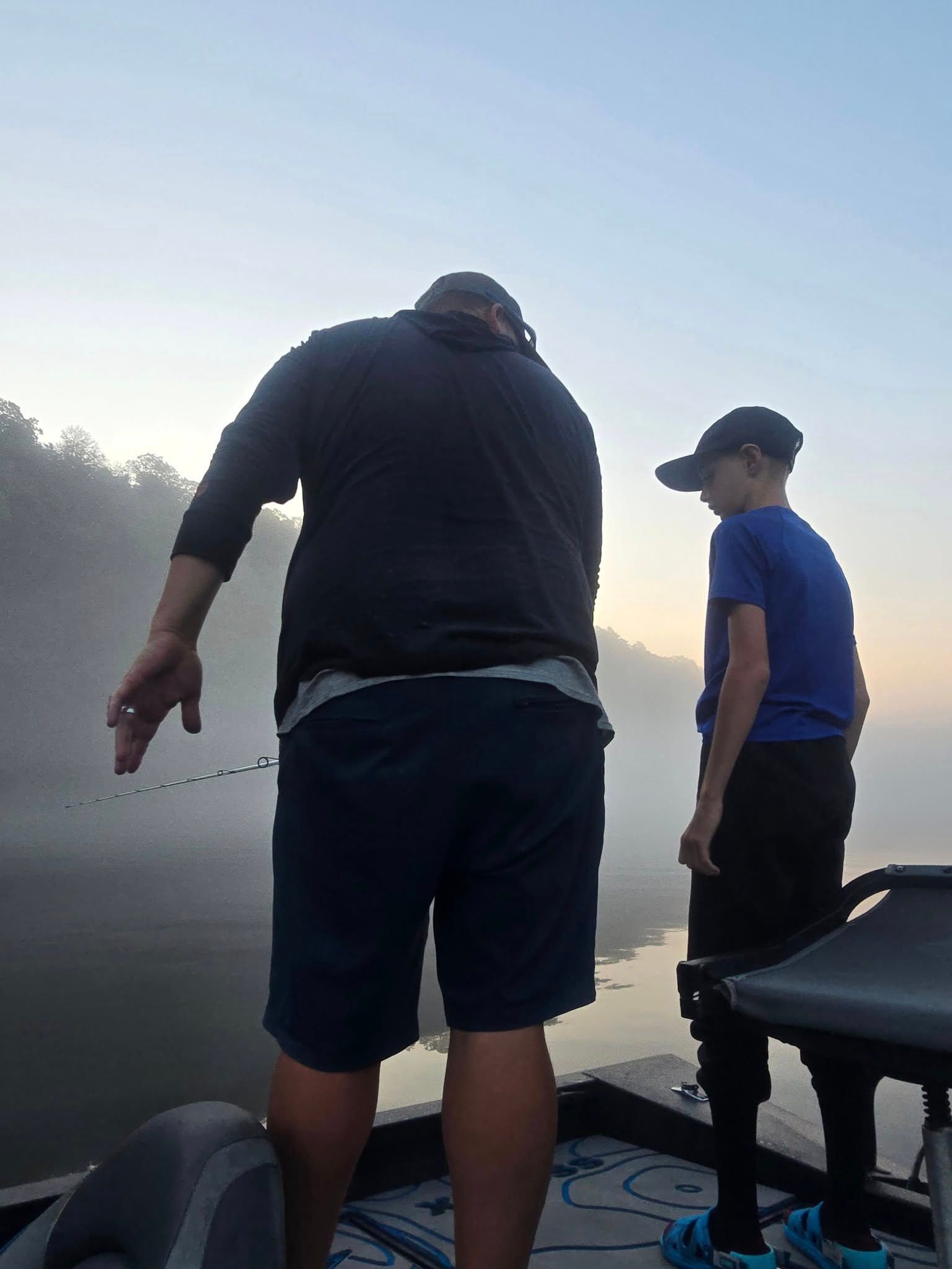 Two people fishing from a boat on misty water during early morning