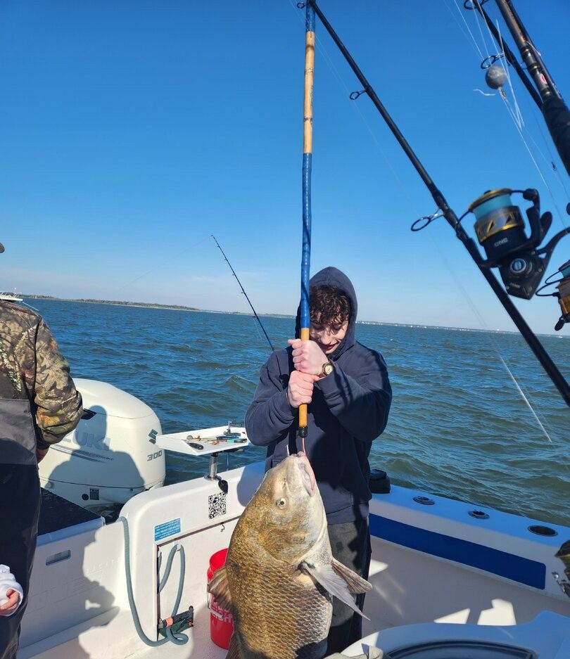 Large fish caught on fishing rod being held up on boat deck over blue water