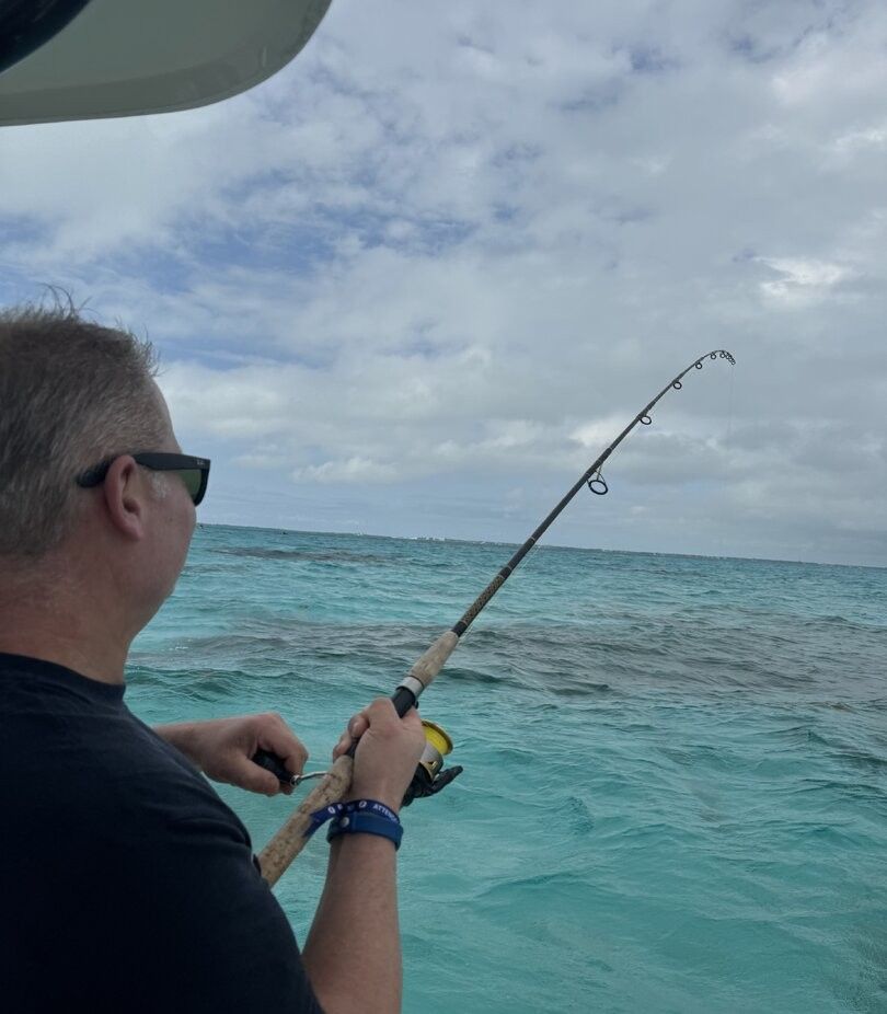 Deep sea fishing with bent rod indicating fish on the line in clear turquoise waters