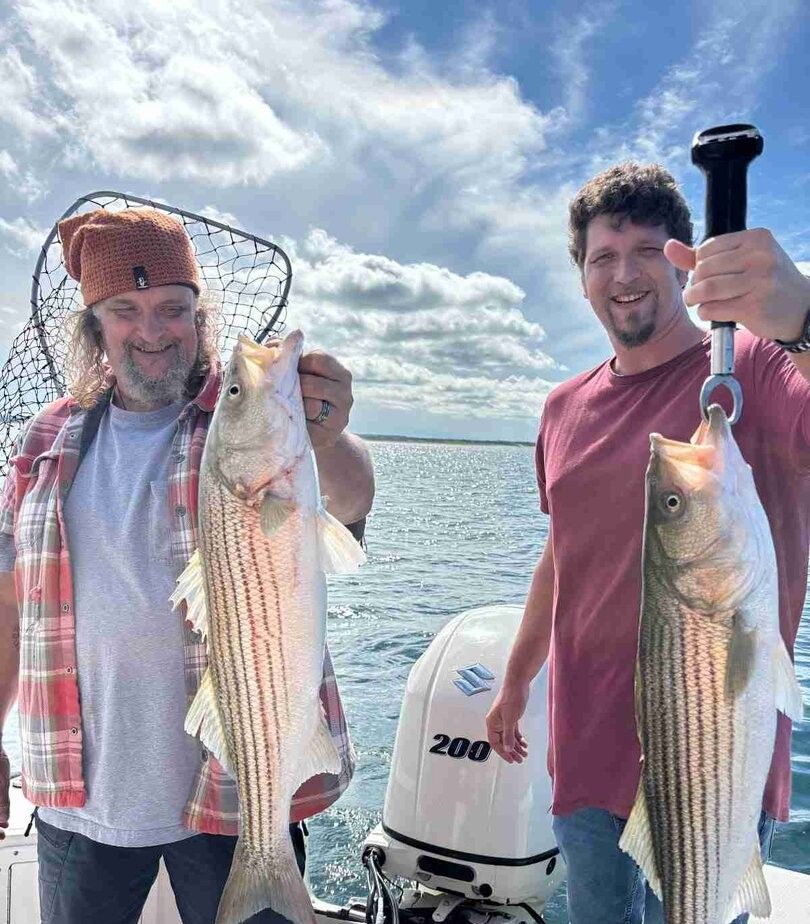 Two striped bass caught during fishing trip displayed with fishing net and equipment on boat