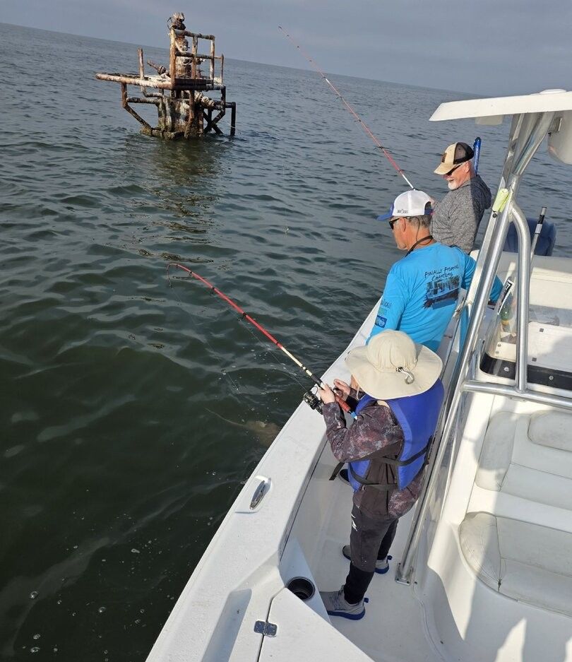 Fishing boat with multiple anglers casting lines near an old offshore structure in open water