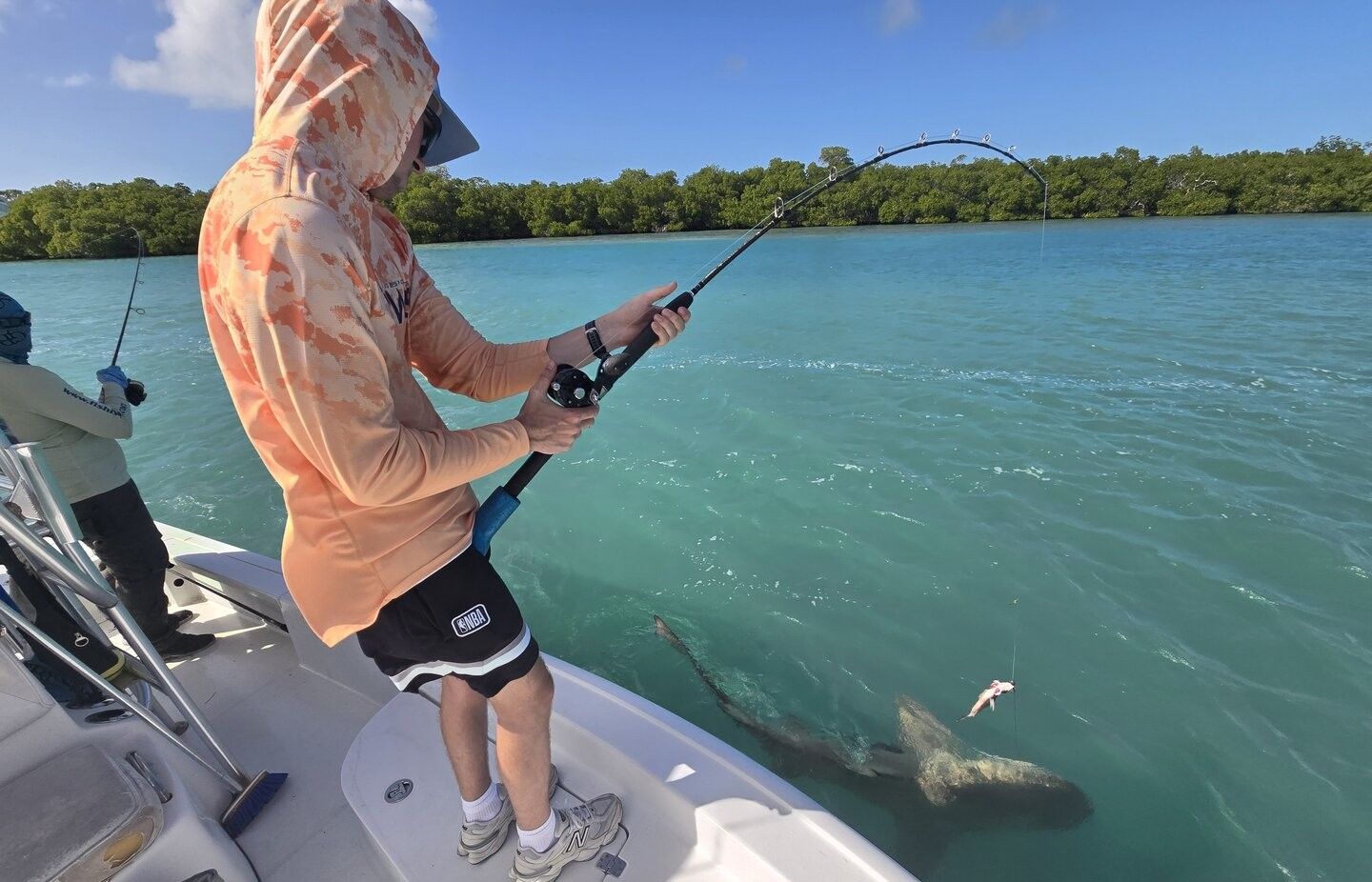 Fishing rod bent while fighting fish from boat on clear water