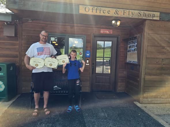 Two people standing outside office and fly shop holding certificates