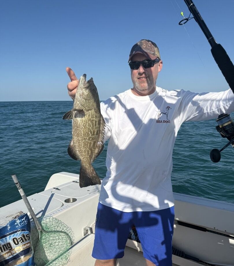 Angler holding freshly caught gag grouper on fishing boat deck with ocean backdrop