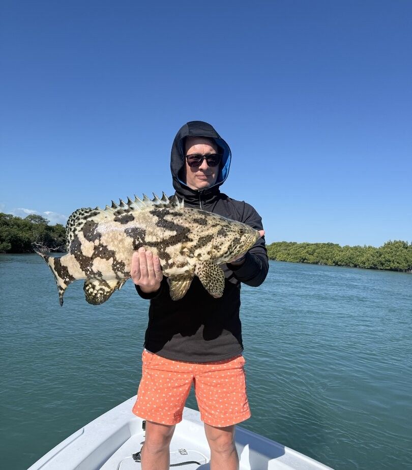 Angler holding large Goliath Grouper on fishing boat in coastal waters