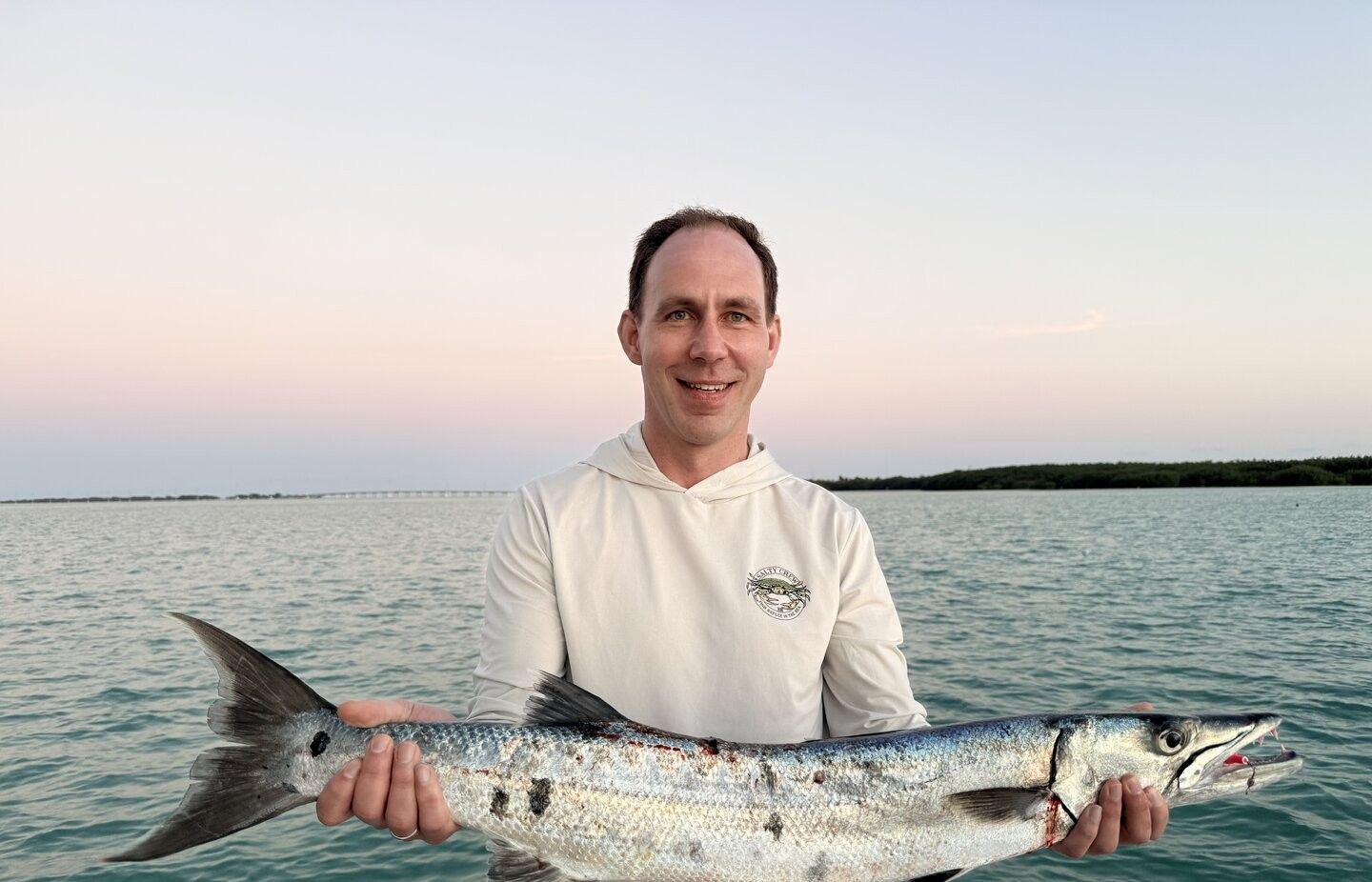 Angler holding a caught great barracuda on a boat with water in the background