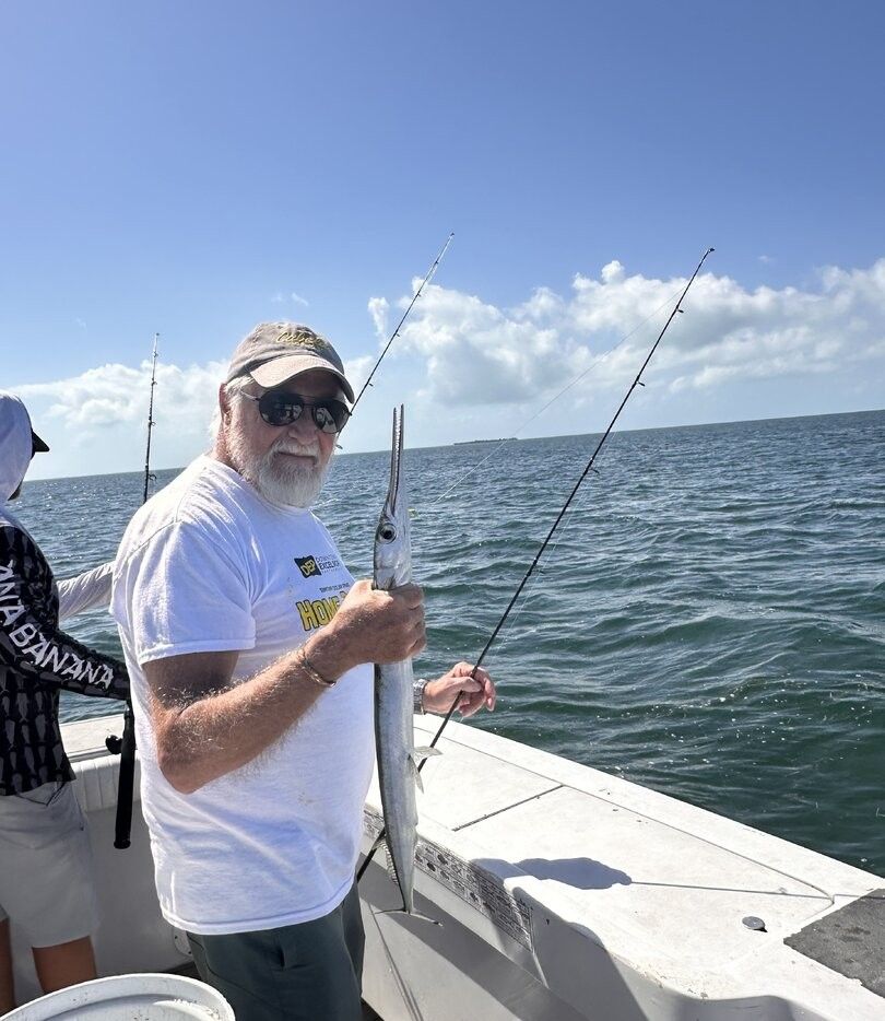 Angler holding freshly caught houndfish on fishing boat with multiple fishing rods