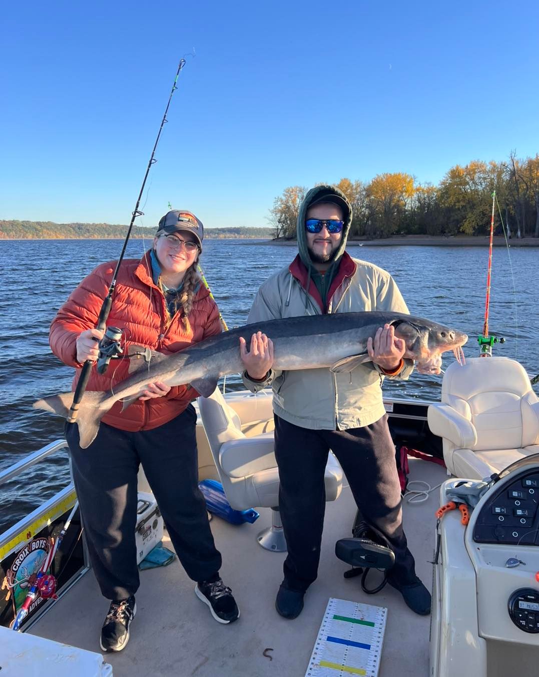Two anglers holding a large lake sturgeon on a fishing boat