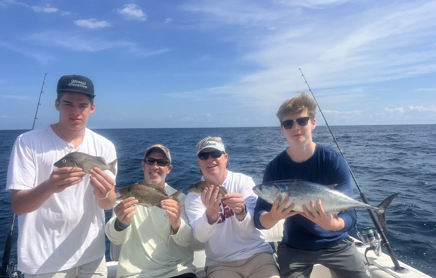 Four anglers displaying their catch of three fish species including little tunny on fishing boat