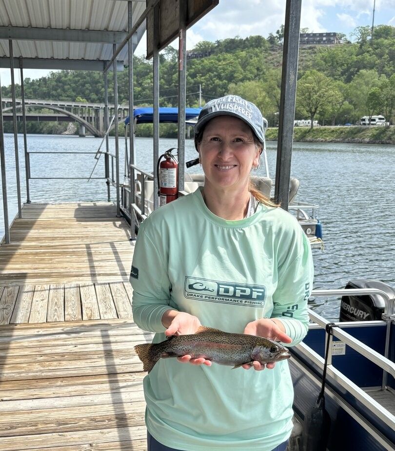 Angler holding freshly caught rainbow trout on wooden dock with lake and bridge in background