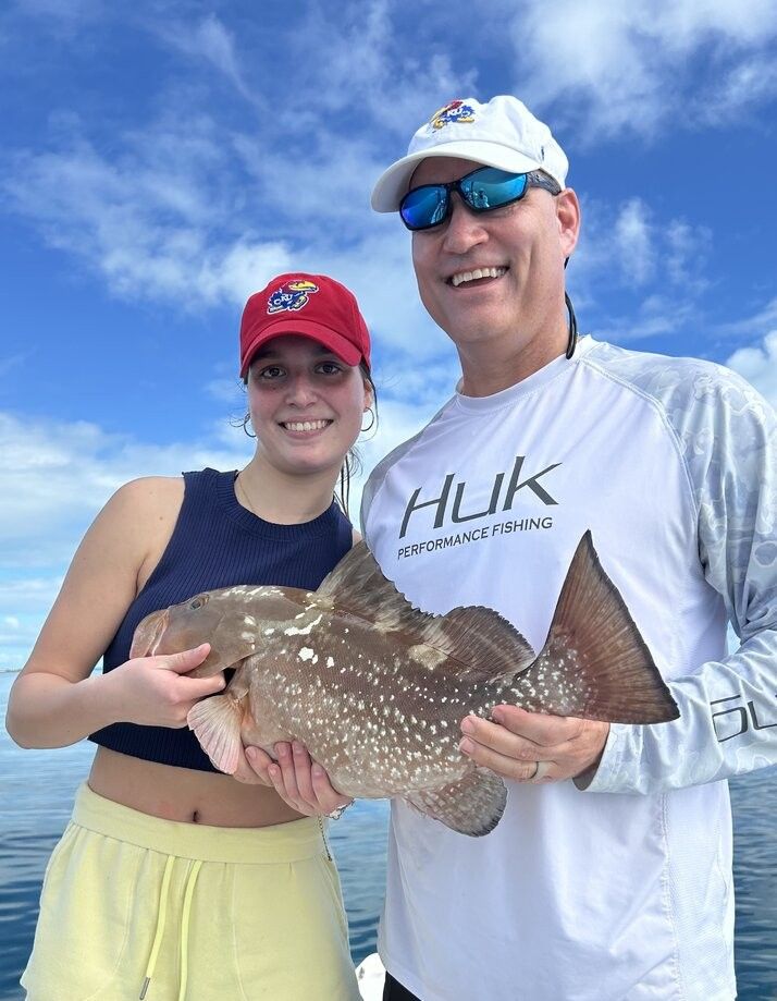 Red grouper catch displayed on fishing boat with ocean and cloudy sky in background
