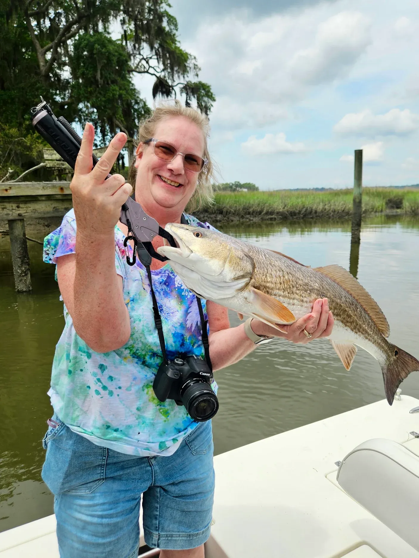 Angler holding caught redfish on boat dock with water and trees in background