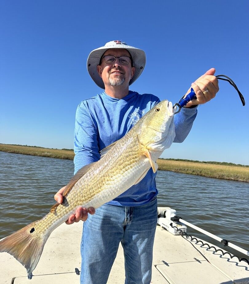 Angler holding large redfish on boat deck with fishing rod
