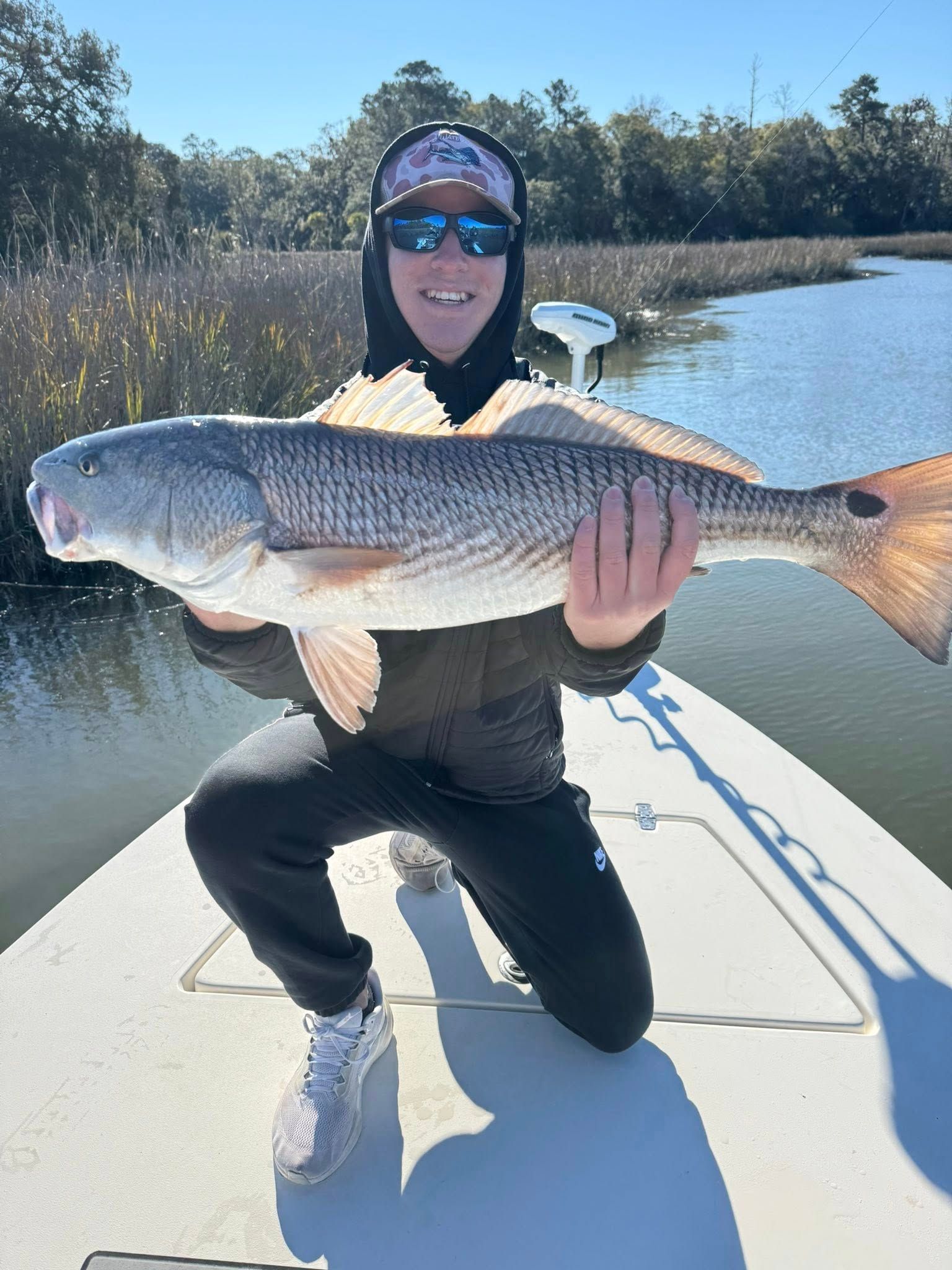 Angler holding caught redfish on boat in shallow water with marsh grass background