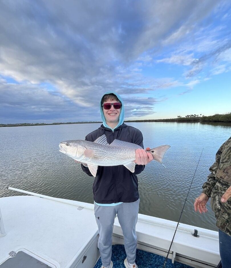 Angler holding large redfish catch on fishing boat with calm water and cloudy sky in background
