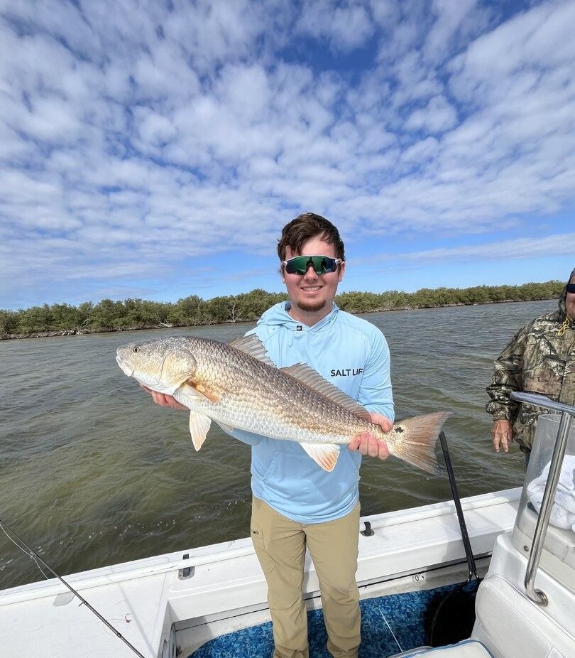 Freshly caught redfish being displayed on fishing boat with water and trees in background