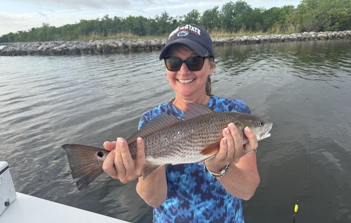 Angler holding freshly caught redfish on fishing boat with water and rocky shoreline in background