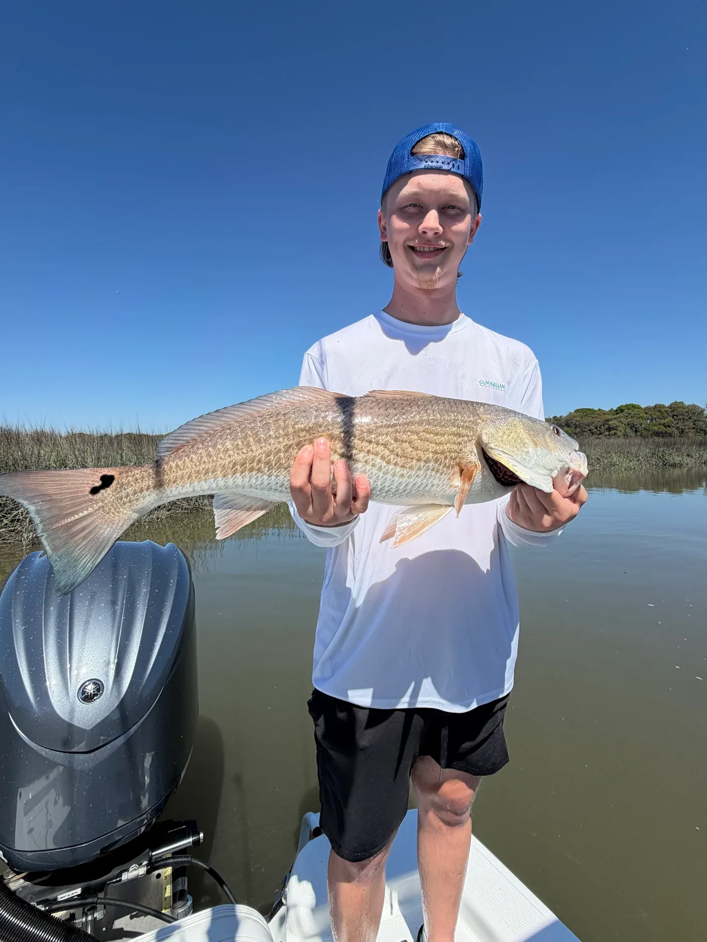 Angler holding caught redfish on fishing boat in shallow water