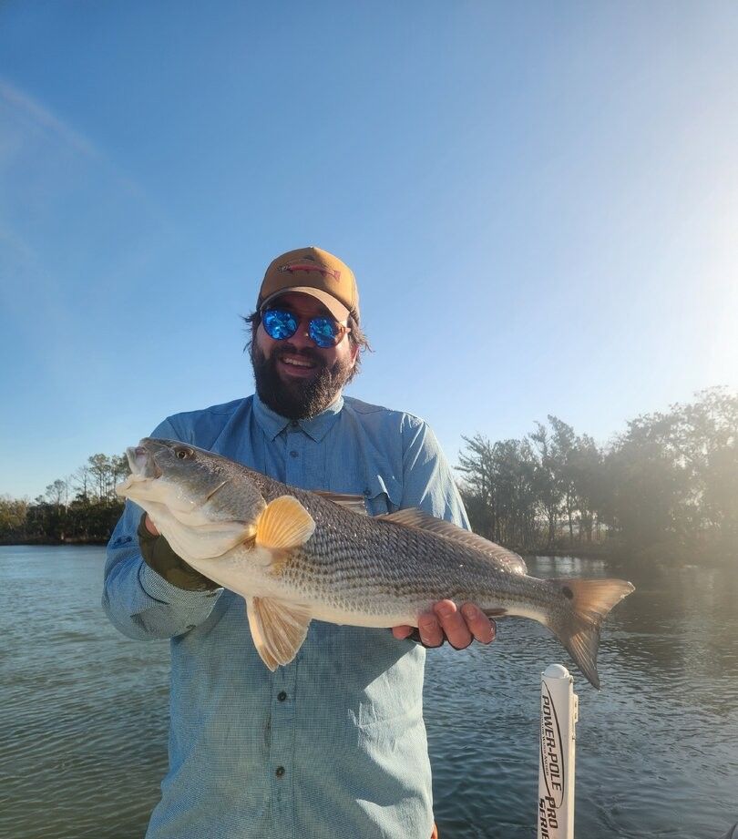 Angler holding caught redfish on boat with water and trees in background
