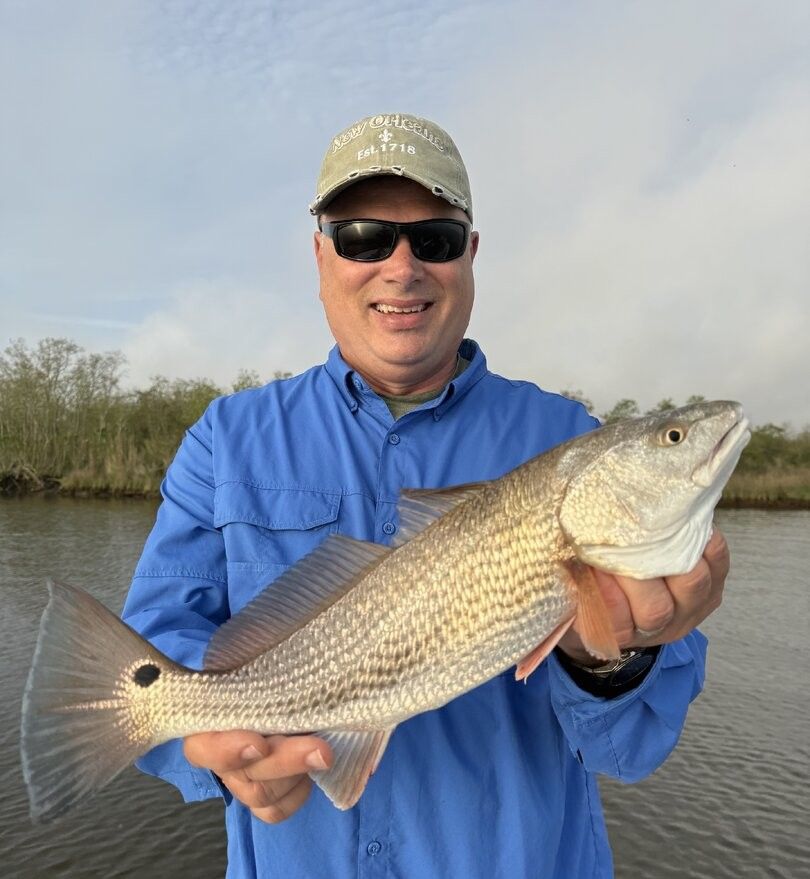 Angler holding caught redfish on water with marsh grasses in background