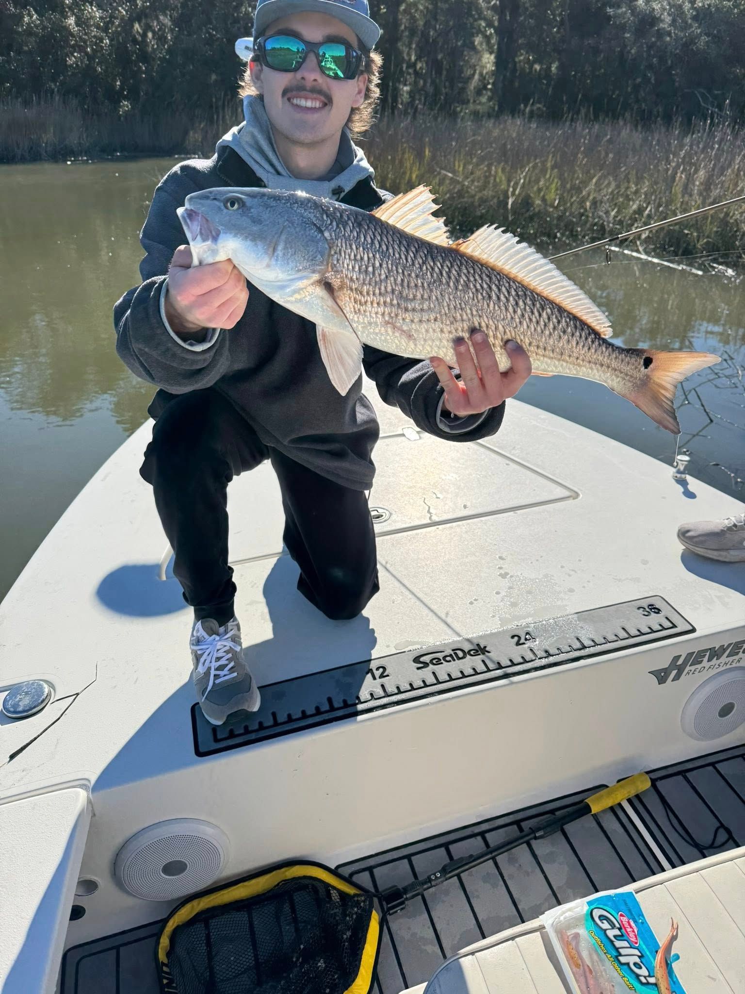 Angler holding freshly caught redfish on fishing boat deck with measuring ruler