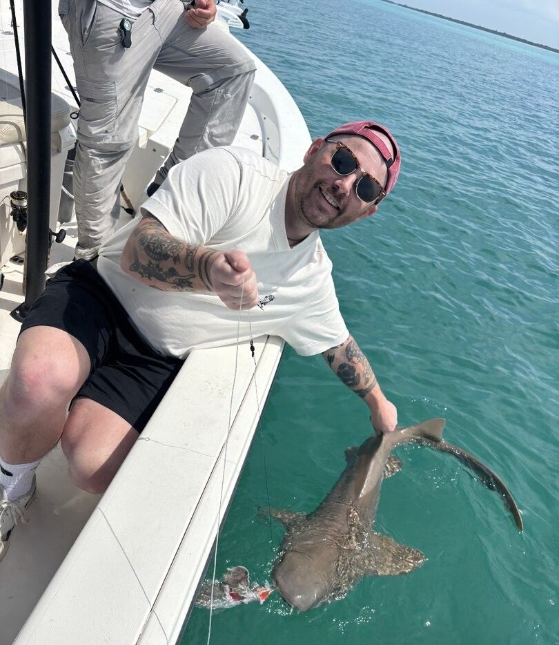 Large shark caught on fishing line next to boat in clear blue water