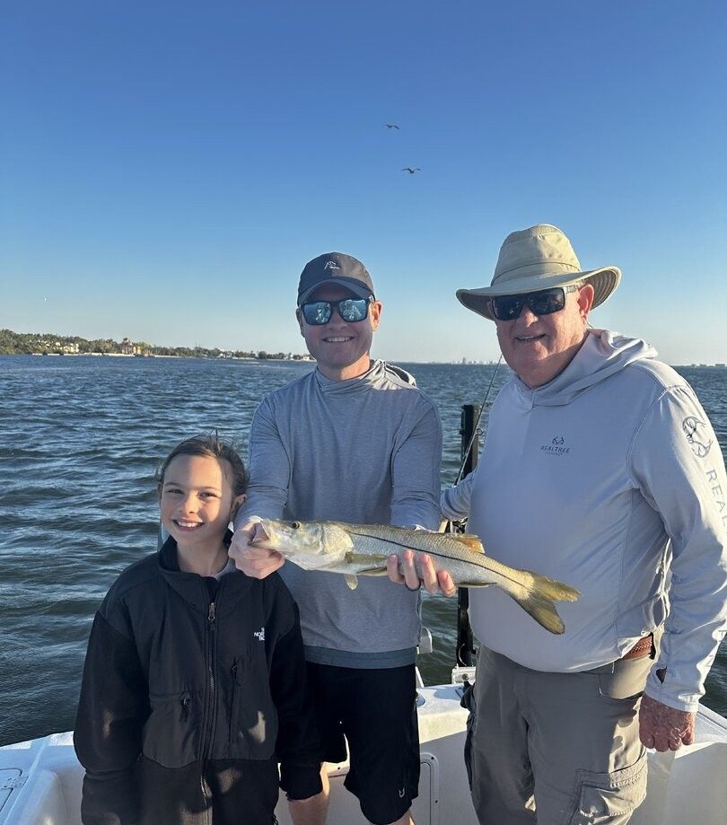 Three people on a fishing boat holding a freshly caught snook on the water