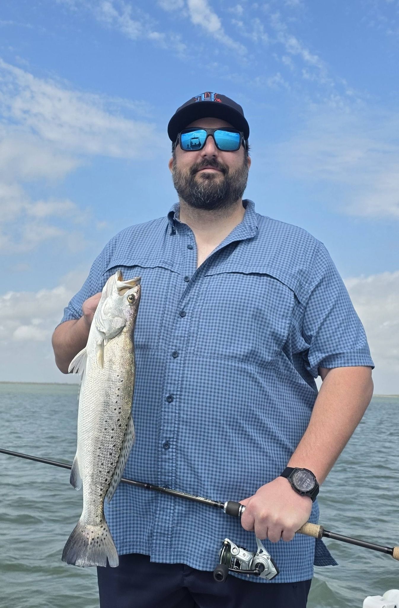 Angler holding freshly caught speckled trout with fishing rod on open water