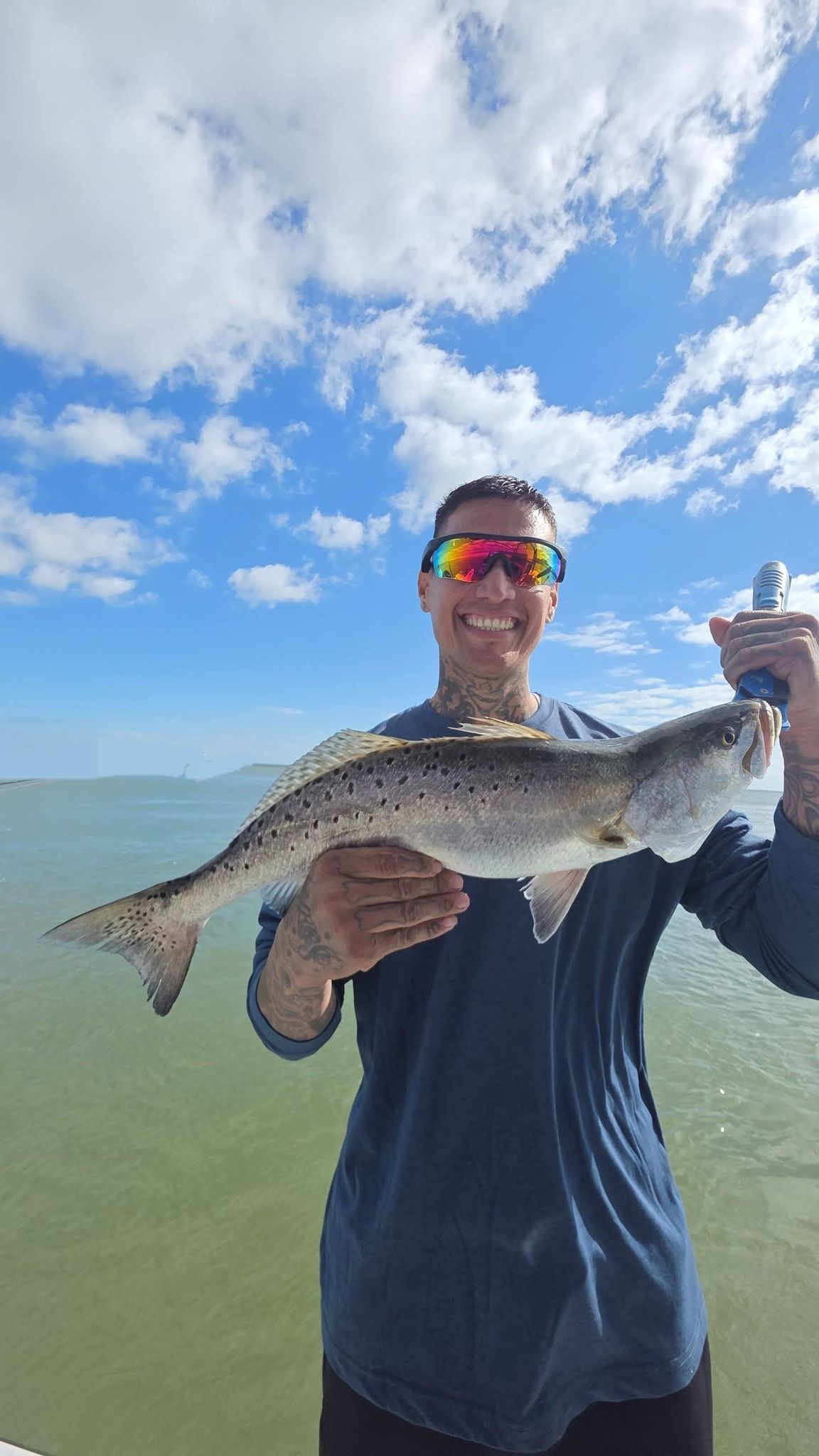 Angler holding freshly caught speckled trout while fishing in shallow coastal waters