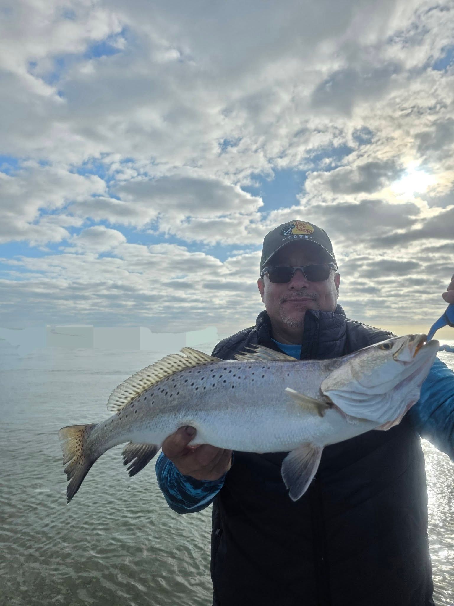 Angler holding freshly caught speckled trout on fishing charter boat with cloudy sky background