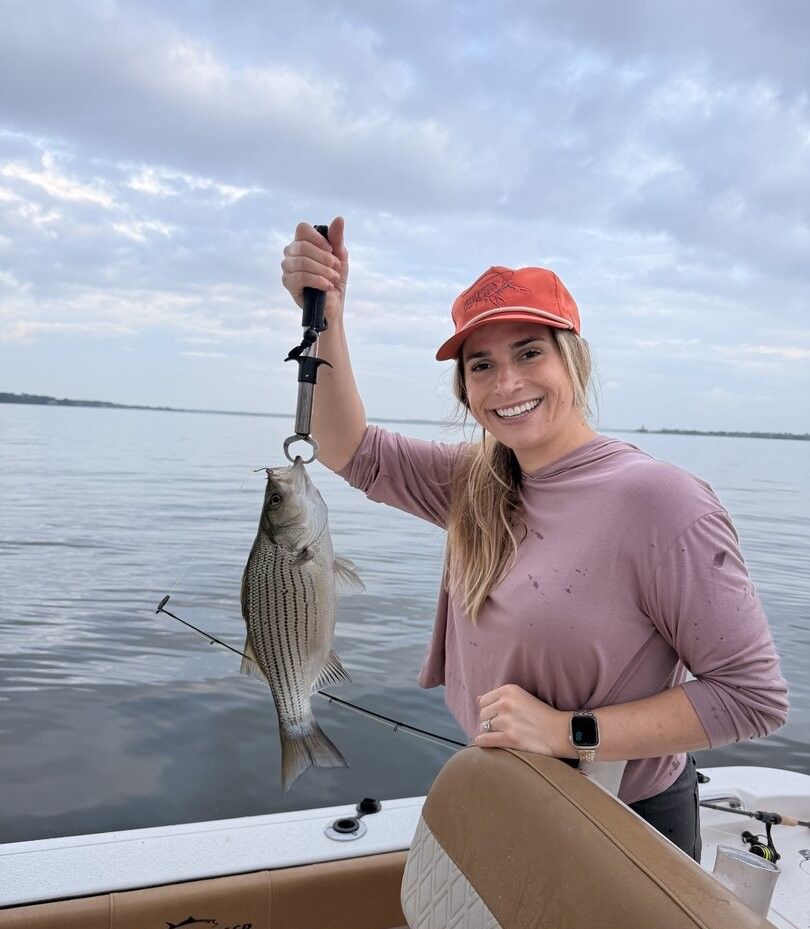 Angler holding caught striped bass on fishing boat