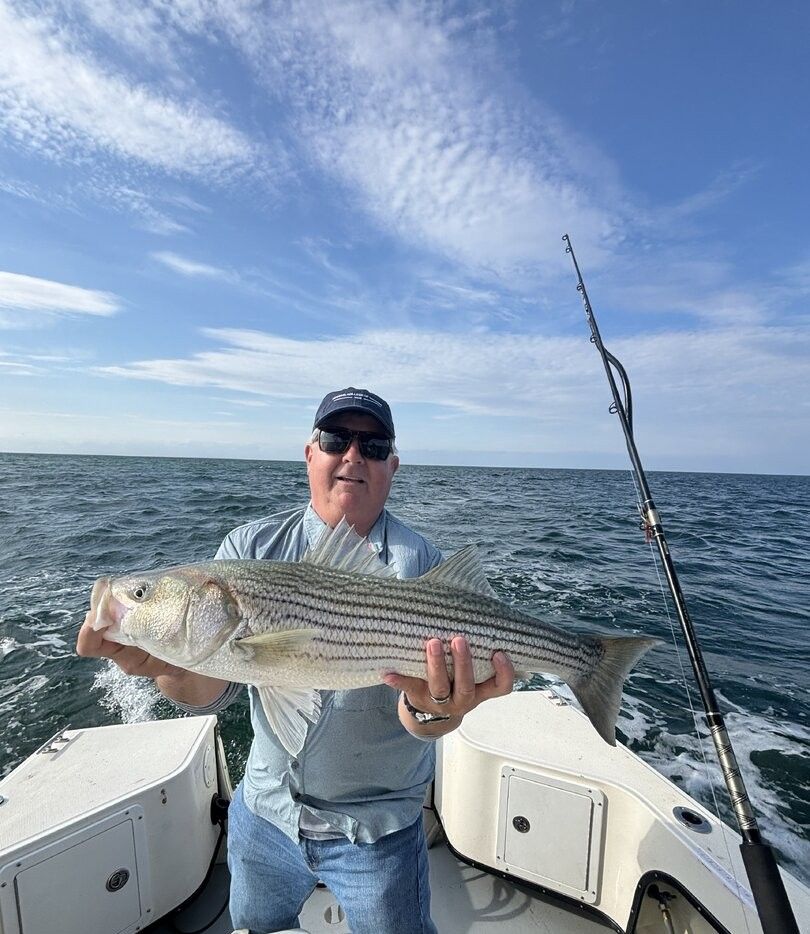 Angler holding striped bass on fishing boat in ocean