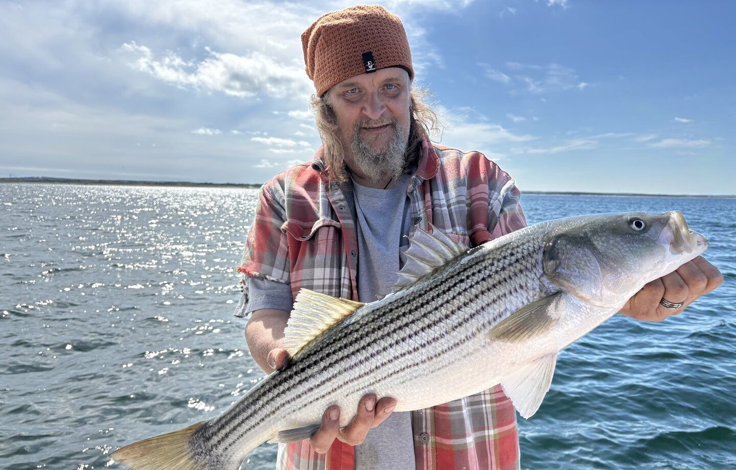 Angler holding large striped bass caught while fishing on open water